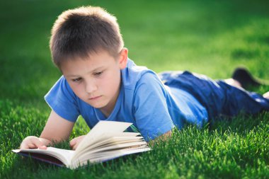Yeşil çimenlerin üzerinde uzanmış kitap okuma çocuk 