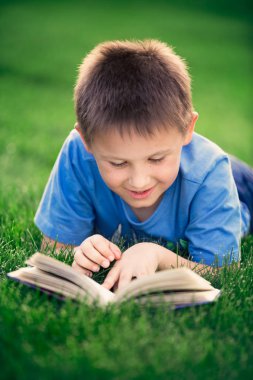 Yeşil çimenlerin üzerinde uzanmış kitap okuma çocuk 