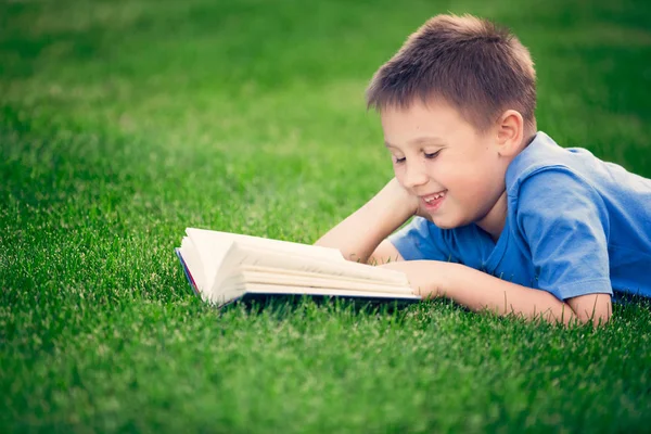 Boy reading book, lying down on green grass — Stock Photo, Image