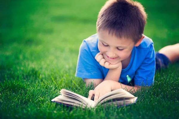 Boy reading book, lying down on green grass — Stock Photo, Image