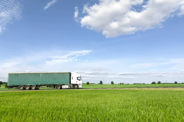 道路を走る輸送トラック青い空の緑の牧草地 — ストック写真