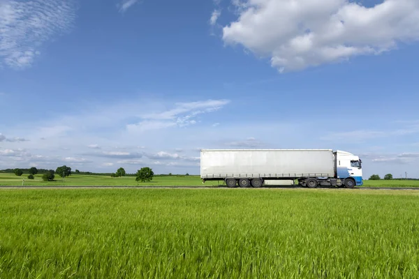 transport truck driving on the road, green meadow with blue sky