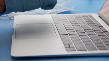 Tıbbi laboratuvar teknisyeni koruyucu lateks eldivenler giyip elinde kan örneğiyle test tüpü tutuyor ve hasta bilgilerini dizüstü bilgisayarla giriyordu, 4K