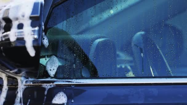 スポンジやシャンプーで車を洗う 濡れた暗い車のクローズアップで手の泡を広げる — ストック動画