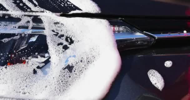 用海绵和洗发水洗车 用手把泡沫撒到前灯车上 — 图库视频影像