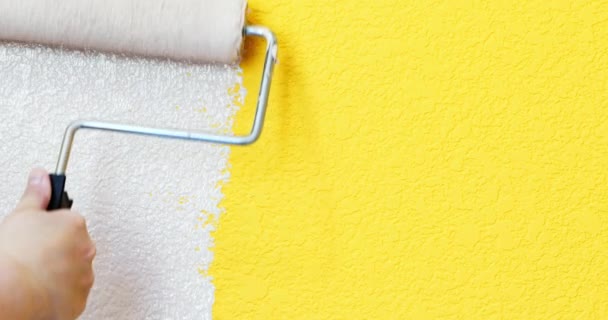 ハンドローラーを使用した絵画 黄色の壁のクローズアップ上に白い塗料を描く 新鮮な色で部屋の改装 — ストック動画