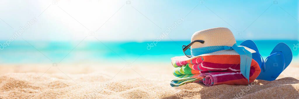 Beach accessories straw hat, flip flops, towel on sunny tropical beach, summer holidays vacation, Caribbean beach with turquoise water background