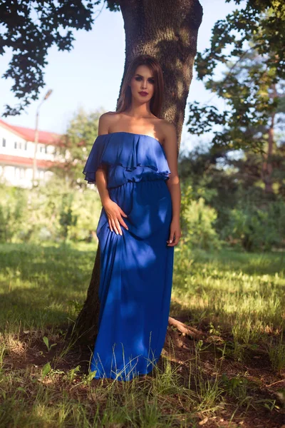 Frau in blauem Kleid lehnt an Baum — Stockfoto