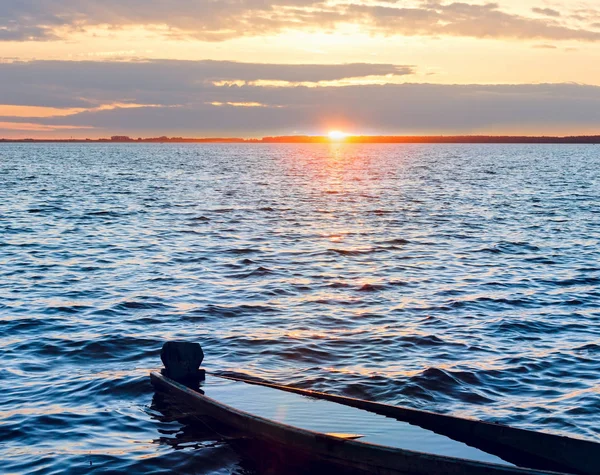 Закат и утонувшая лодка на берегу озера — стоковое фото
