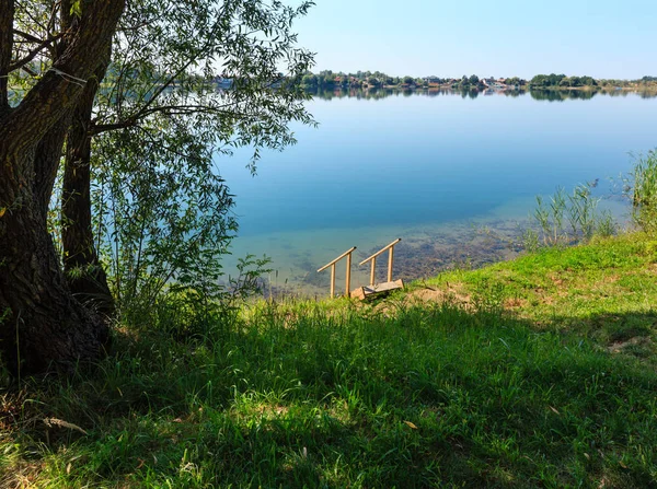 Lago de verano playa tranquila con madera se inclina hacia el agua — Foto de Stock