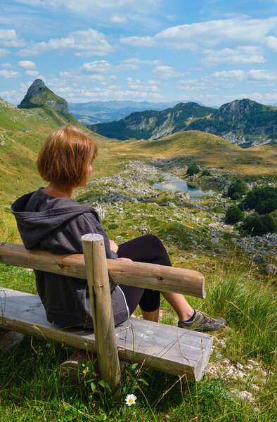 Женщина на деревянной скамейке и живописном летнем горном ландшафте национального парка Дурмитор, Черногории, Европы, Балканских Динарских Альп, Всемирного наследия ЮНЕСКО. Панорамная дорога Дурмитор, перевал Седло
.