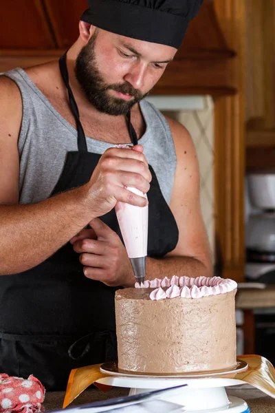 ストロベリームースのフリストでチョコレートの誕生日ケーキを飾る男性パン屋 — ストック写真