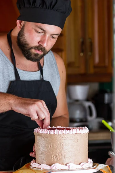ストロベリームースのフリストでチョコレートの誕生日ケーキを飾る男性パン屋 — ストック写真