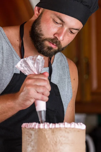 ストロベリームースのフリストでチョコレートの誕生日ケーキを飾る男性パン屋 — ストック写真