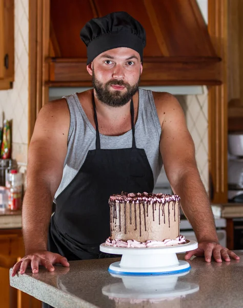young pastry chef in his home kitchen presenting a just made and decorated birthday cake with chocolate frosting and strawberry mouse.