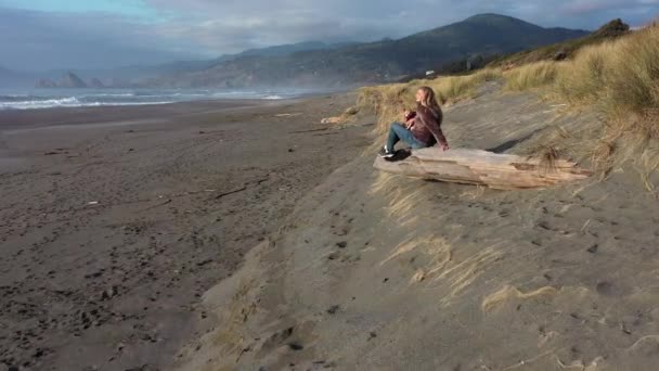 オレゴン海岸の草原の砂丘のドリフトログに座って — ストック動画