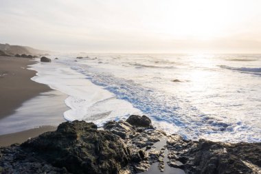 Nesika Sahili, Oregon 'da kayalık kıyı şeridi, öğleden sonra güneş ufka doğru yaklaşırken ince bir bulut tabakası boyunca.