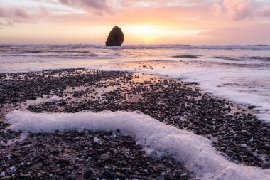 Gold Beach Oregon 'da gün batımı sahnesi. Renkli bulutlar ve dalgalar ıslak kum ve kayalara yansıyan renkler ekliyor.