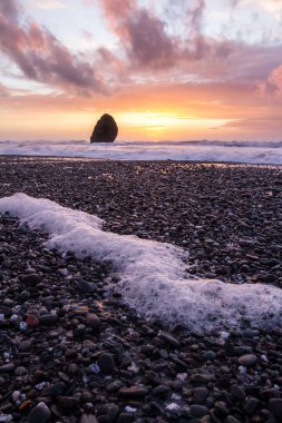 Gold Beach Oregon 'da gün batımı sahnesi. Renkli bulutlar ve dalgalar ıslak kum ve kayalara yansıyan renkler ekliyor.