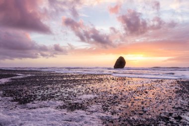 Gold Beach Oregon 'da gün batımı sahnesi. Renkli bulutlar ve dalgalar ıslak kum ve kayalara yansıyan renkler ekliyor.