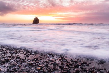 Gold Beach Oregon 'da gün batımı sahnesi. Renkli bulutlar ve dalgalar ıslak kum ve kayalara yansıyan renkler ekliyor.