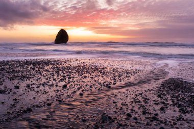 Gold Beach Oregon 'da gün batımı sahnesi. Renkli bulutlar ve dalgalar ıslak kum ve kayalara yansıyan renkler ekliyor.