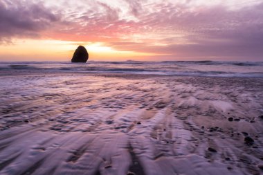 Gold Beach Oregon 'da gün batımı sahnesi. Renkli bulutlar ve dalgalar ıslak kum ve kayalara yansıyan renkler ekliyor.