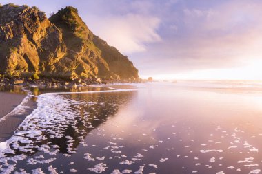 Güneş ufkun altına batarken Güney Oregon sahillerindeki manzaraya parlaklık ve renk katarken, altın ışık Cape Sebastian 'daki kayalara yansıyor.