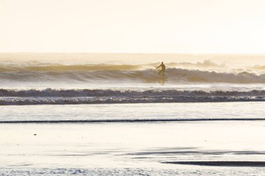 Güneş batarken Oregon sahilinin soğuk sularında sörf yapmak sise ve havaya güçlü bir ışık ve neme bir ışık katar.