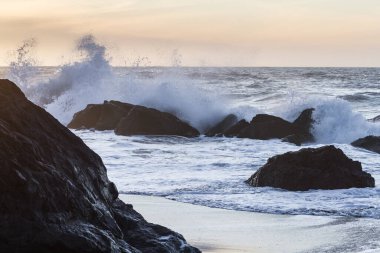 Nesika Sahili, Oregon 'daki Rocky kıyı şeridi. Öğleden sonra güneş ufka yaklaşırken dalgalar kayalara çarpıyor.