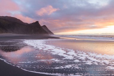Oregon sahilindeki muhteşem günbatımı sahnesi ıslak kumlara, dalgalara ve Oregon 'un güney sahillerindeki Cape Sebastian tepelerine yansıyan renkli bulutlarla birlikte.