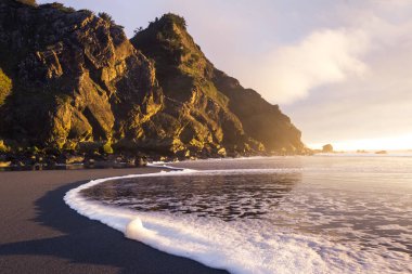 Güneş ufkun altına batarken Güney Oregon sahillerindeki manzaraya parlaklık ve renk katarken, altın ışık Cape Sebastian 'daki kayalara yansıyor.