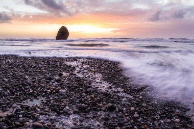 Gold Beach Oregon 'da gün batımı sahnesi. Renkli bulutlar ve dalgalar ıslak kum ve kayalara yansıyan renkler ekliyor.