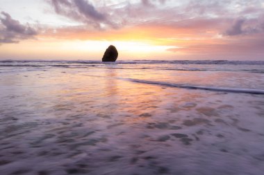 Gold Beach Oregon 'da gün batımı sahnesi. Renkli bulutlar ve dalgalar ıslak kum ve kayalara yansıyan renkler ekliyor.