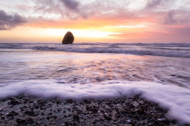 Gold Beach Oregon 'da gün batımı sahnesi. Renkli bulutlar ve dalgalar ıslak kum ve kayalara yansıyan renkler ekliyor.