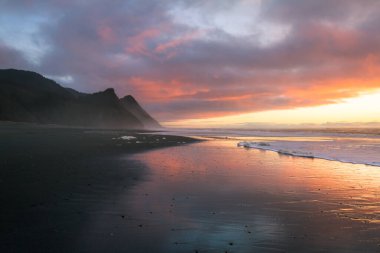 Oregon sahilindeki muhteşem günbatımı sahnesi ıslak kumlara, dalgalara ve Oregon 'un güney sahillerindeki Cape Sebastian tepelerine yansıyan renkli bulutlarla birlikte.