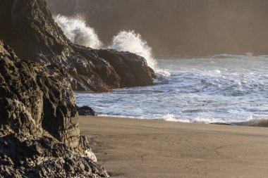 Güneş, Oregon 'daki Gizli Plaj' da bir kaya sandığı yarışmasına çarpan bir dalgayı aydınlatırken parlak bir sıçrama.