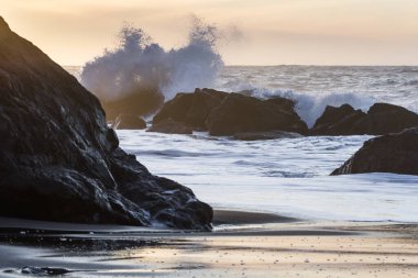 Nesika Sahili, Oregon 'daki Rocky kıyı şeridi. Öğleden sonra güneş ufka yaklaşırken dalgalar kayalara çarpıyor.