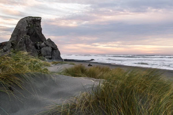 太陽が地平線に沈み 暗い雲に色を加え オレゴン海岸にある砂や草に光を当てる美しいシーン — ストック写真