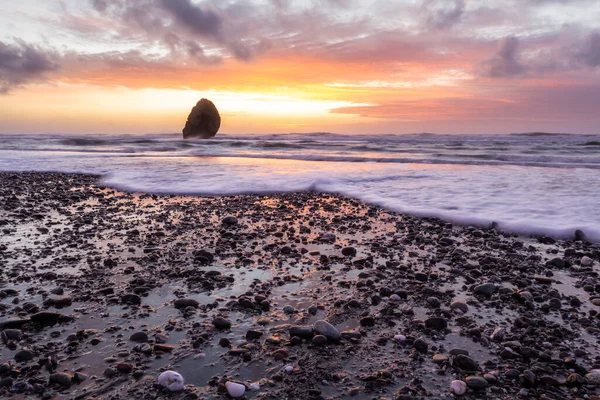 Gold Beach Oregon 'da gün batımı sahnesi. Renkli bulutlar ve dalgalar ıslak kum ve kayalara yansıyan renkler ekliyor.