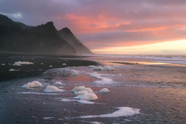 Gorgeous sunset scene in the Oregon coast with colorful clouds reflecting on the wet sand and waves and the hills of Cape Sebastian in the southern Oregon coast