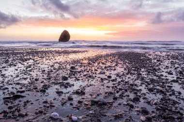 Gold Beach Oregon 'da gün batımı sahnesi. Renkli bulutlar ve dalgalar ıslak kum ve kayalara yansıyan renkler ekliyor.