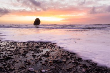Gold Beach Oregon 'da gün batımı sahnesi. Renkli bulutlar ve dalgalar ıslak kum ve kayalara yansıyan renkler ekliyor.