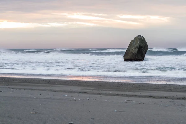 当海浪在俄勒冈州海岸的一块巨大岩石上冲撞时 地平线上的夕阳西下 美丽的风景给乌云增添了色彩 — 图库照片