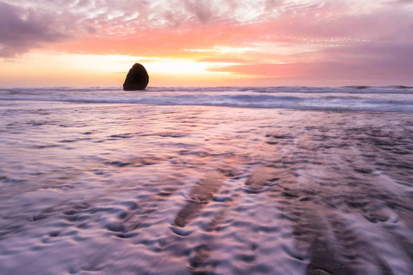 Gold Beach Oregon 'da gün batımı sahnesi. Renkli bulutlar ve dalgalar ıslak kum ve kayalara yansıyan renkler ekliyor.