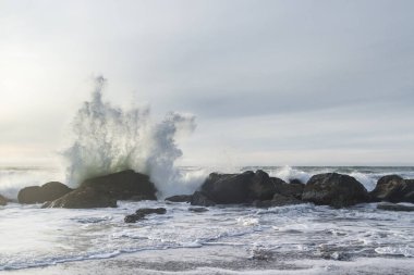 Nesika Sahili, Oregon 'daki Rocky kıyı şeridi. Öğleden sonra güneş ufka yaklaşırken dalgalar kayalara çarpıyor.