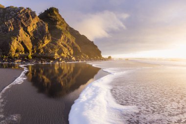 Güneş ufkun altına batarken Güney Oregon sahillerindeki manzaraya parlaklık ve renk katarken, altın ışık Cape Sebastian 'daki kayalara yansıyor.
