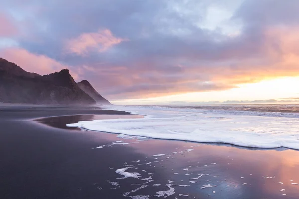 Gorgeous sunset scene in the Oregon coast with colorful clouds reflecting on the wet sand and waves and the hills of Cape Sebastian in the southern Oregon coast