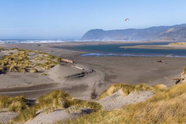 Pistol Nehri 'nin ağzında sörf yapan bir uçurtma. Güney Oregon' un arka planında engebeli bir kıyı var.