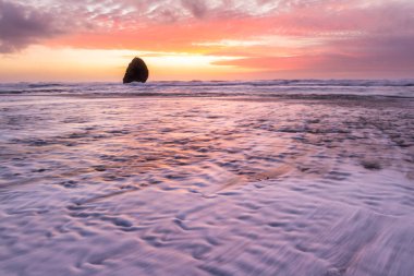 Gold Beach Oregon 'da gün batımı sahnesi. Renkli bulutlar ve dalgalar ıslak kum ve kayalara yansıyan renkler ekliyor.